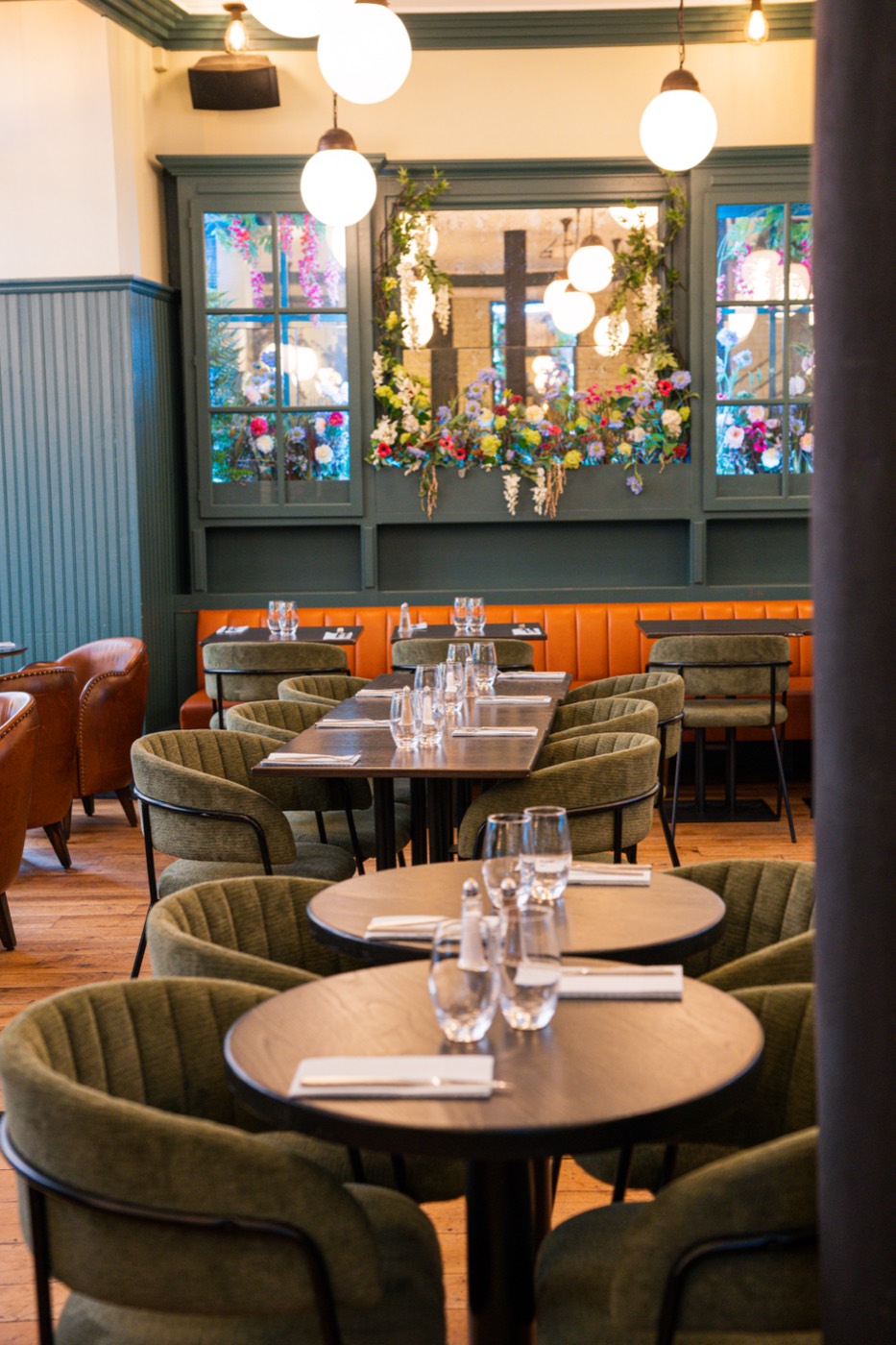 Banquette orange et tables dressées sous les vitrines fleuries, Bistrot Jad