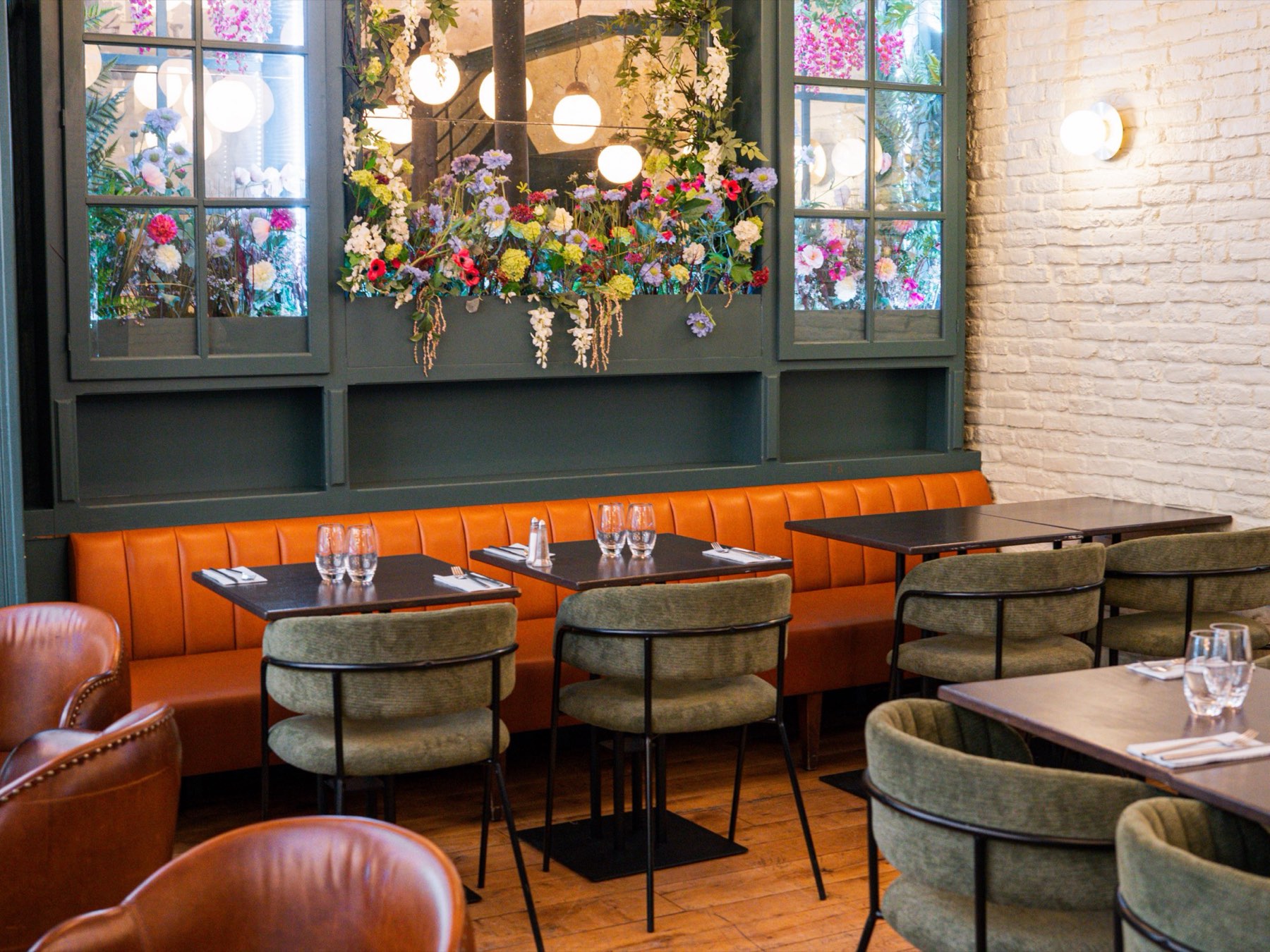 Salle du Bistrot Jad : vitrines vertes fleuries, banquette orange et fauteuils en cuir cognac