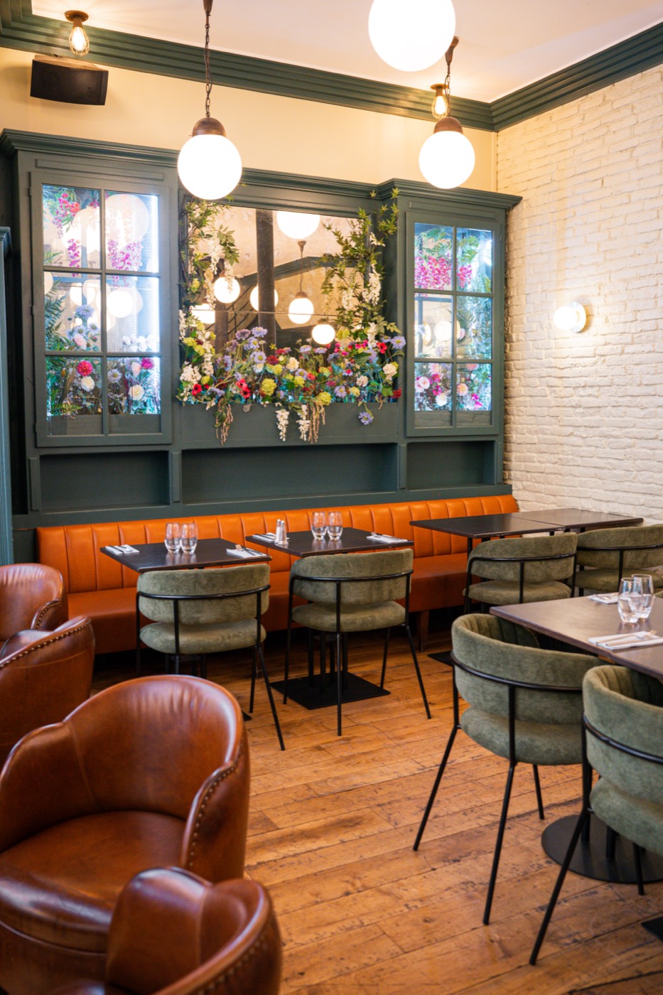 Vitrines vertes fleuries et fauteuils en cuir cognac du Bistrot Jad